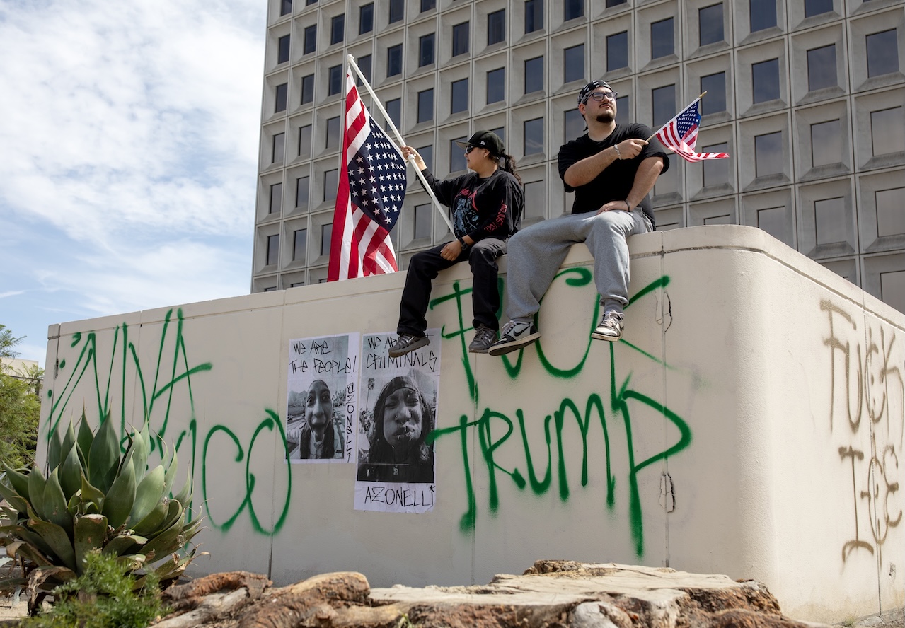 Two protesters on a graffiti-covered wall during the "No Kings" protest against Donald Trump in downtown Los Angeles.